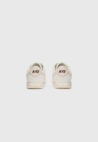 Nike kedai off-white ādas, ar noapaļotu formu, teksturētām akcentiem un tumši brūnu logotipu uz papēža.