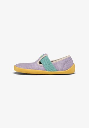 Lawendowy but typu slip-on z żółtą podeszwą i szerokim turkusowym elastycznym paskiem na wierzchu, wykonany z miękkiej, teksturowanej tkaniny.