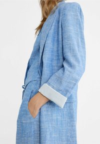 Lichtblauwe linnen blazer met een relaxte fit, voorzien van gestreepte manchetten, open voorkant en een zak, die een gestructureerde stof benadrukt.