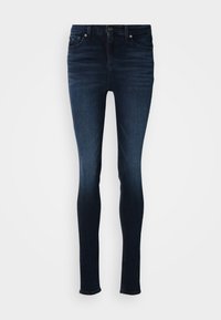 Skinny jeans in dark denim, featuring a mid-rise waist, five-pocket design, and metallic button closure. Smooth texture with minimal fading.