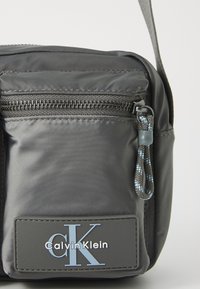 Czarna nylonowa torba na ramię z zamykaną kieszenią, plecionym uchwytem oraz naszywką z logo "Calvin Klein".