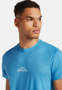 Camiseta de manga corta azul claro hecha de tejido suave, que presenta un logotipo blanco de Icebreaker con un diseño de montaña en el pecho.