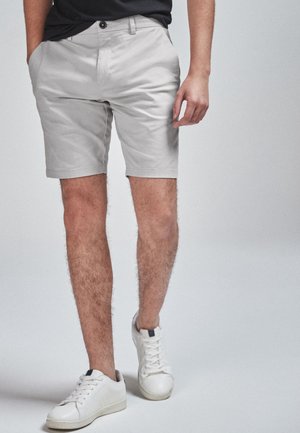 Shorts en coton gris clair avec poches latérales, devant plat et ourlet revers. Portés avec des baskets blanches et une chemise noire.