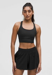 Zwarte sportbeha met een brede halslijn en dikke banden, gecombineerd met zwarte shorts met elastische taille die een losse pasvorm en zachte stofkwaliteit hebben.