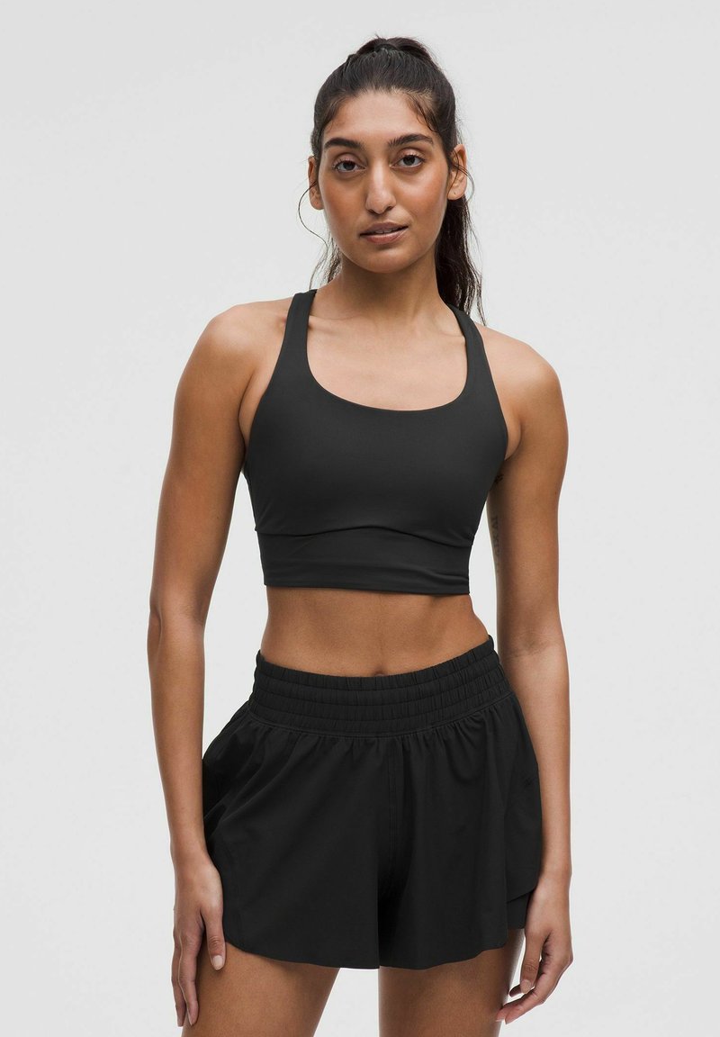 Zwarte sportbeha met een brede halslijn en dikke banden, gecombineerd met zwarte shorts met elastische taille die een losse pasvorm en zachte stofkwaliteit hebben.