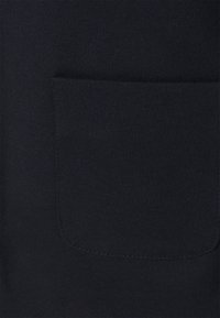 Navy-Pulloverstoff mit einer vorderen aufgesetzten Tasche und sichtbaren Nähten. Die Textur ist glatt und leicht dehnbar.