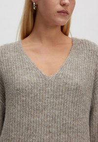 V-Ausschnitt-Pullover aus einem hellbeigen strukturierten Strick. Verfügt über rippierte Stoffe und eine lässige Passform, die das weiche, gemütliche Material hervorhebt.