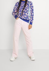 Pull avec une base bleue et imprimé léopard rose, associé à un pantalon évasé rose clair et des baskets blanches. Un sac à main remarquable ajoute un contraste de couleurs.