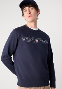 Námořnický sweatshirt vyrobený ze 100% bavlny, s kulatým výstřihem, dlouhými rukávy a předním grafickým vzorem s textem a pruhy. Hladká textura.