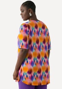 Túnica colorida con un patrón de tie-dye en tonos naranja, púrpura y azul. Las mangas cortas y el dobladillo redondeado aportan un ajuste relajado.