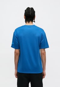 Camisola atlética azul de manga curta, material de poliéster, textura suave, gola de crew ribanda, logótipo na manga direita, barra reta.