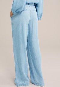 Los pantalones anchos de mezclilla azul claro presentan una cintura alta, bolsillos delanteros y bolsillos traseros tipo parche, con una textura suave y un ajuste relajado.