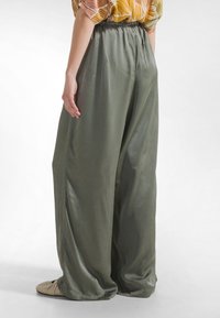 Olivenfarvede bukser med vide ben lavet af et glat, satinlignende stof. Med elastisk talje og flydende silhuet.
