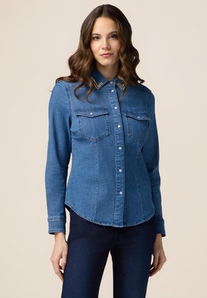 Cămașă din denim cu guler ascuțit, accente asemănătoare perlelor, două buzunare la piept și închidere cu nasturi. Prezintă mâneci lungi și o croială adaptată.