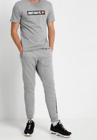 Grå t-shirt med kort ärm och "Just Do It"-logga, ihop med ljusgrå joggingbyxor och svarta sneakers med vita sulor och mönstrade snören.