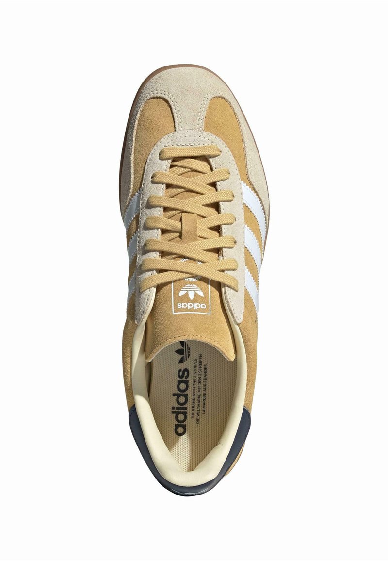 Tanfarbene Wildledersneaker mit weißen Streifen, runder Zehenform und flachen Schnürsenkeln. Mit einem Logo auf der Zunge und einem kontrastierenden dunklen Absatz.