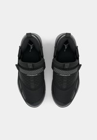 Chaussures de sport noires avec une tige en mesh et texturée, des sangles réglables et un accent à pois. Logo visible à l'avant.