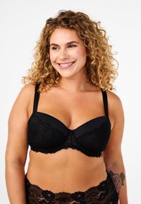 Reggiseno in pizzo nero e rete con coppe imbottite, spalline regolabili e sovrapposizione in pizzo floreale per una texture dettagliata.