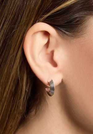 Silver hoop earrings with a spiral design, featuring multiple stacked bands. The texture is smooth, and they are worn in the ear.
