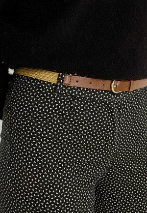 Pantalones negros con estampado de triángulos crema, combinados con un cinturón de cuero marrón con hebilla dorada y textura tejida.