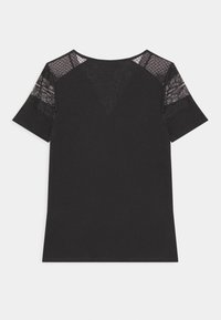 Chemise noire à manches courtes avec des panneaux en dentelle sur les épaules et les manches supérieures, tissu uni en dessous, posée à plat sur un fond blanc.