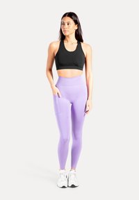 Sort sports-bh med rund halsudskæring, kombineret med højtaljede lavendel-løbebukser med sidelomme, begge lavet af strækbart stof.