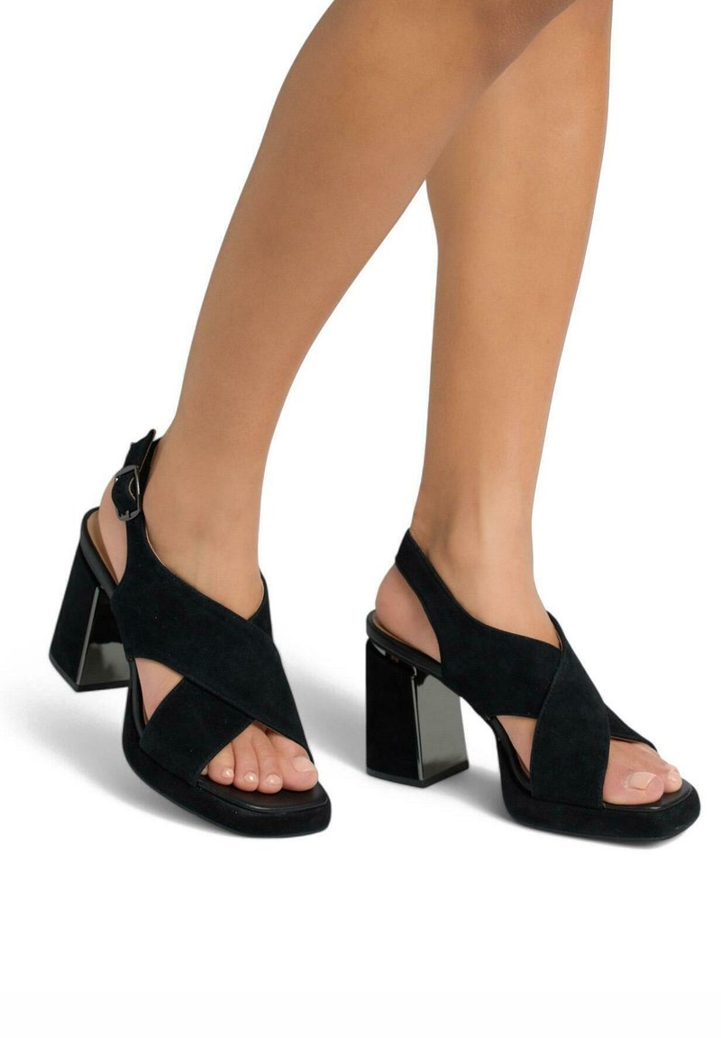 Sandales à talons blocs en daim noir avec design à brides croisées, bout ouvert et boucle de cheville ajustable. Vue latérale mettant en avant la forme moderne.
