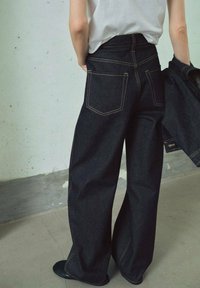Donkerdenim spijkerbroek met een wijde pasvorm, voorzien van gele stiksels, twee achterzakken en een hoge taille. Gladde textuur, stevig materiaal.