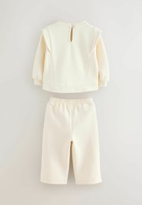 Svetlý krémový dvojdielny set pozostávajúci z topu s dlhým rukávom a zapínaním na zips na zadnej strane a koordinujúcich šortiek s elastickým pásom.