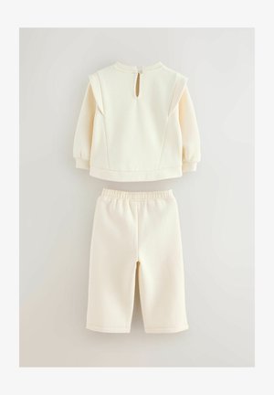 Vaaleankermainen kahden osan setti, joka koostuu pitkät hihnat sisältävästä topista, jossa on vetoketju takana, sekä yhteensopivista shortseista, joissa on joustava vyötärö.