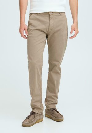 Beige cotton chinos with a straight-leg fit, featuring a zip fly, front pockets, and back pockets, paired with gray suede shoes.