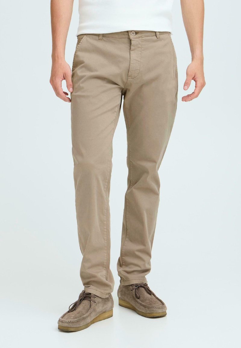 Beige cotton chinos with a straight-leg fit, featuring a zip fly, front pockets, and back pockets, paired with gray suede shoes.