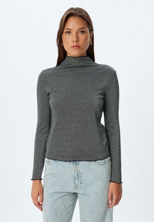 Top ajustado de color gris con cuello alto, confeccionado en un material de canalé texturizado, con mangas largas y dobladillo con forma de puntilla, combinado con jeans de color azul claro.