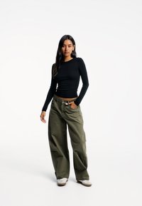 Long-sleeve black top paired with loose-fitting olive green pants and white sneakers. The outfit features a simple design and neutral colors.
