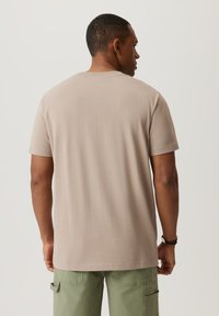 Beżowa bawełniana koszulka z okrągłym dekoltem, krótkimi rękawami i prostym krojem, widoczna z tyłu, zestawiona z zielonymi spodniami cargo.