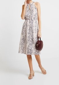Halters neck dress in snake print, featuring a keyhole detail and an elastic waist. Worn with a burgundy handbag and beige block-heel sandals.