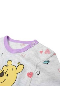 T-shirt bébé en coton gris avec un col violet, orné d'un graphisme de ours jaune ludique et de cœurs roses et bleus sur tout le tissu.