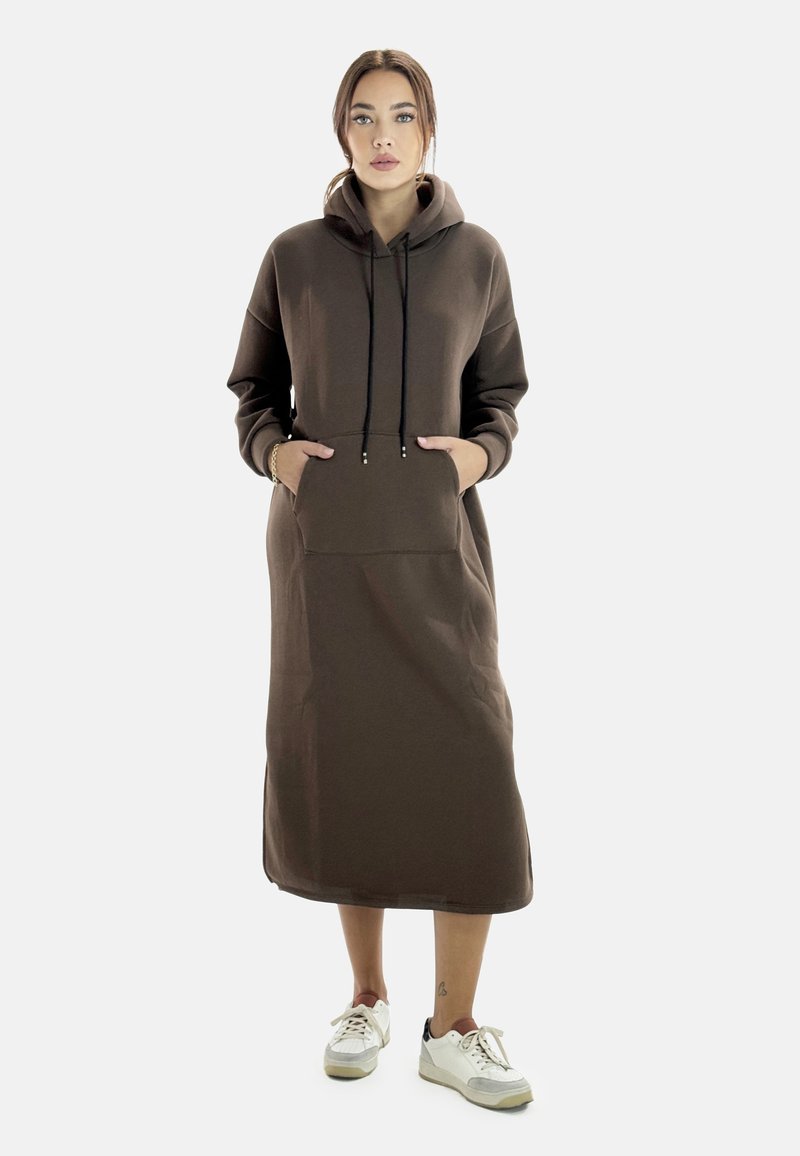 Abito sudato con cappuccio in marrone, maniche lunghe, tasca a marsupio e coulisse. Materiale morbido e design fino al ginocchio. Indossato con sneaker bianche.