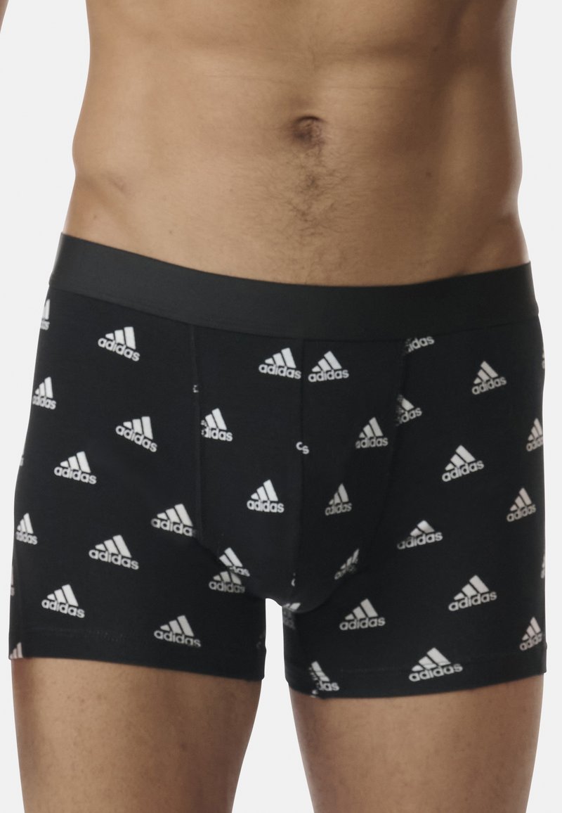 Boxer in cotone elasticizzato neri con un elastico liscio, caratterizzati da un motivo ripetuto del logo Adidas bianco su tutta la superficie.