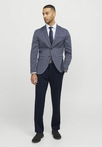 Blazer gris à carreaux avec deux boutons, accompagné d'une chemise blanche et d'un pantalon marine. Des chaussures noires complètent cette tenue formelle.