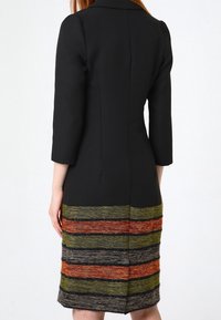 Svart klänning med trekvartslånga ärmar; strukturerad design med en texturerad, flerfärgad randig nederdel i grönt, orange och grått.