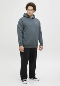 Grå hoodie med en frontlomme, der har et lille logo. Kombineret med sorte lige bukser og sorte sneakers med hvide detaljer.