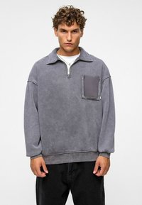 Grijze pullover sweatshirt met een ritssluiting aan de kraag, een voorzak en geribde manchetten. Zachte textuur, losse pasvorm en casual ontwerp.