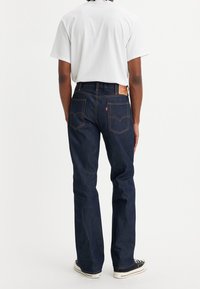 Jeans en denim bleu foncé avec une coupe décontractée, dotés d'une poche arrière, de deux poches arrière et de coutures contrastantes orange. Portés avec un t-shirt blanc.