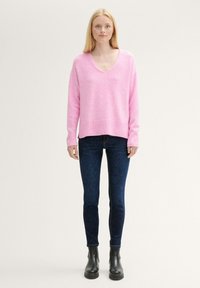 Rosa stickad tröja med V-ringning, långa ärmar och ribbad fåll, kombinerad med mörkblå skinny jeans och svarta ankelstövlar.