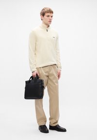 Beige half-zip sweater, black leather briefcase, beige trousers, and black shoes worn by a young adult. Simple design with minimal accents.