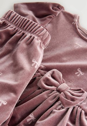 Ljubičasta baršunasta haljina s skupljenim rukavima i pojasom, koja ima veliki ukras u obliku mašne i male uzorke mašni po cijeloj haljini. Glatka tekstura.