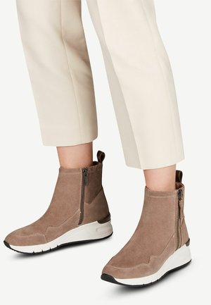 Bruine suède enkellaarzen met een witte zool, voorzien van ritsen aan de zijkant en een ronde neus. Gecombineerd met cropped crème broek.