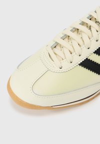 Beige leren sneaker met zwarte strepen, rubberen zool en beige veters. Heeft stiksel details en een gladde afwerking.