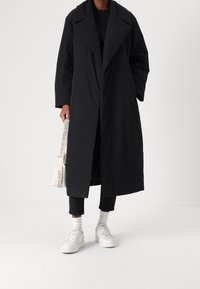 Black long coat with a wide collar, featuring a relaxed fit and a smooth texture, paired with dark jeans and white sneakers.